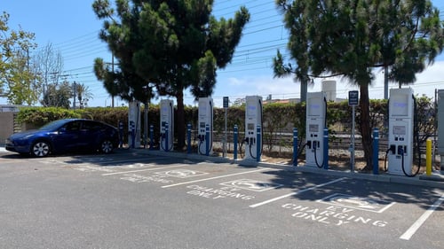 Several EVgo fast charging units installed in marked parking spaces at a public charging station, with EVgo logos on the chargers, protective bollards around each unit. Photo taken midday.