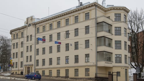 Toimipiste ulkoa: vanha, vaaleankeltainen, viisikerroksinen rakennus kadun varressa. Ulkona on loskaa ja talon edessä liikennevaloihin pysähtynyt auto.
