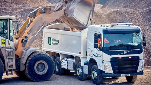 Front loader pours aggregate into a Heidelberg Materials dump truck at a quarry site.