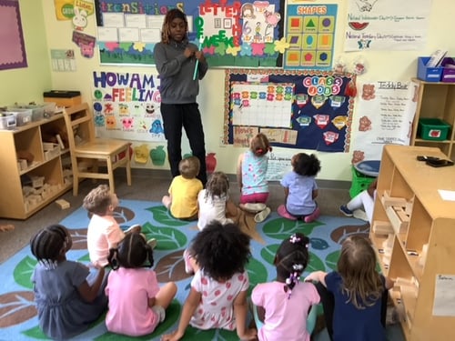 Teacher leading a group of children through a fun, interactive demonstration.