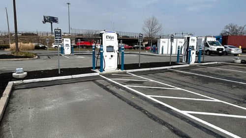 Several EVgo fast-charging units installed in marked parking spaces at a public charging station, with EVgo logos on the chargers, protective bollards around each unit