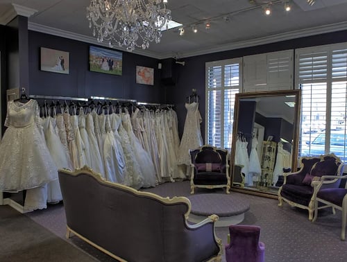 Elegant bridal salon interior with rows of wedding dresses, chandelier lighting, and seating area with mirrors for fittings
