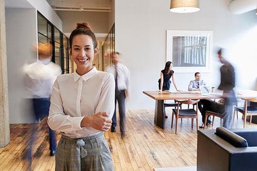 A smiling professional woman stands in a bright, clean, and healthy commercial office environment, representing a successfully restored workspace after property damage remediation.