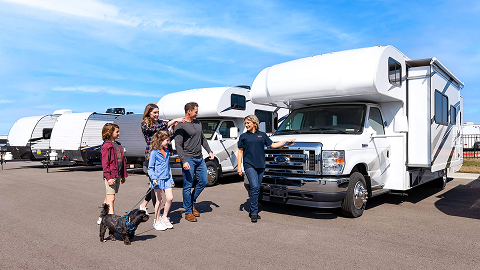 Family walking through an RV lot with a salesman gesturing toward a class C RV
