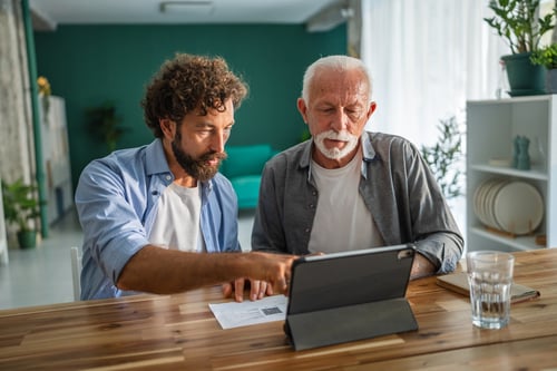 adult son helping senior father on the ipad