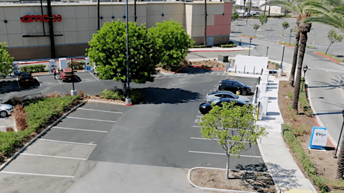 aerial image of a 16 stall evgo charging station. Multiple EVgo fast charging units installed in marked parking spaces at a public charging station, with EVgo logos on the chargers, protective bollards around each unit. NACS and CCS chargers featured in the image.