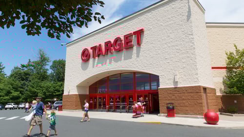 Man and child and person with full shopping cart walking away from Target entrance with trees around