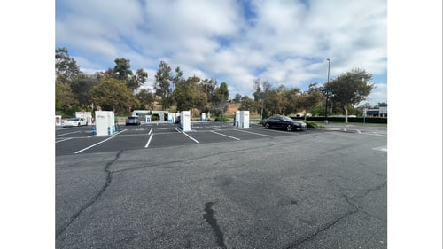Several EVgo fast charging units installed in marked parking spaces at a public charging station, with EVgo logos on the chargers, protective bollards around each unit. CCS chargers featured in the image.