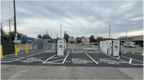 Several EVgo fast-charging units installed in marked parking spaces at a public charging station, with EVgo logos on the chargers, protective bollards around each unit