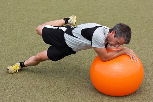 Ein Mann führt eine Balanceübung auf einem großen, orangefarbenen Gymnastikball nach der AFS Functional Training Technik aus im AFD Athletik Studio in Stuttgart.