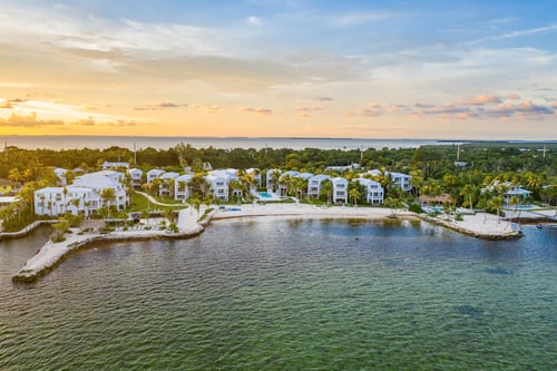 Aerial view of a private marina, private beach, and resort with white buildings and a pool.