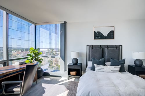 Bedroom at Encore Apartments with city view through expansive windows.