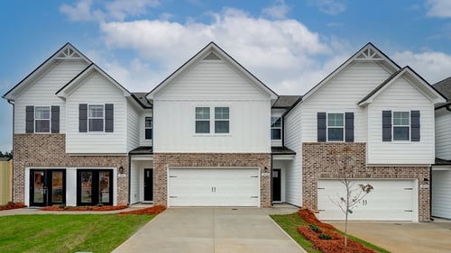 Row of 3 townhomes with 2-car garages with brown brick and white siding at DRB Homes The Borough at Wyndham South
