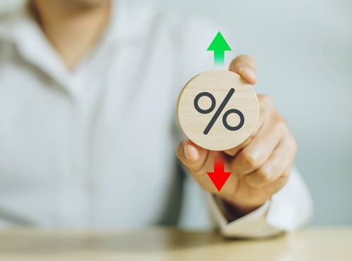 Man holding a percentage sign on a wooden board with red arrow pointing down and green arrow pointing up