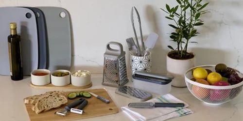 Kitchen utensils and food preparation accessories including graters, chopping board, peeler and fruit bowl