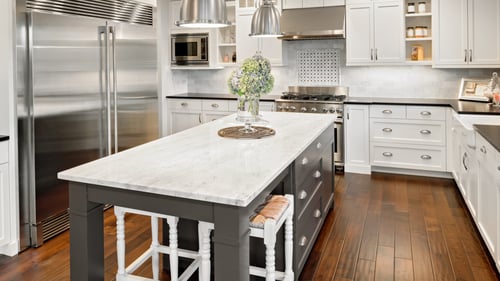 An image of a spacious and modern kitchen featuring a large central island with a polished granite countertop, installed by US Marble & Granite