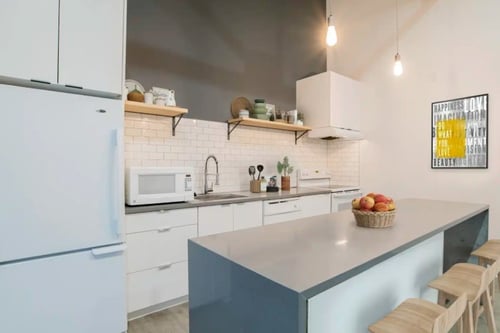 Sleek kitchen with white cabinetry, floating wooden shelves, and a modern gray island.