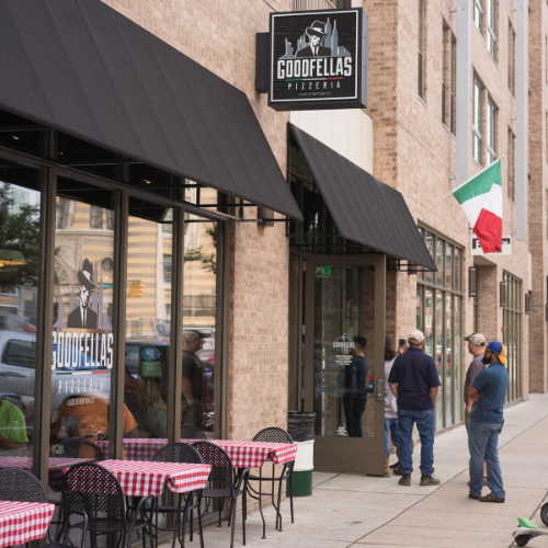 Outdoor tables with red checkered cloths along the sidewalk outside Goodfellas Pizzeria Mass Ave.