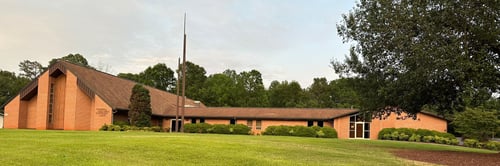 Large grassy area in the foreground with a church building in the background. There are trees behind the building.