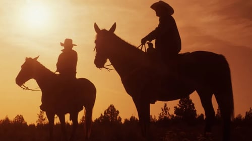 Two people riding horses during sunset