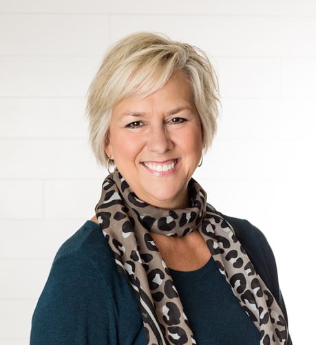 Smiling blonde insurance agent named Heidi Hill wearing a teal sweater with a leopard print scarf.