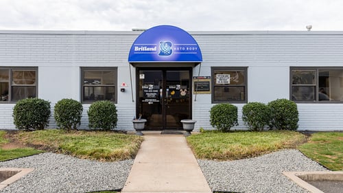 Front entrance of Britland Auto Body in Bridgewater, New Jersey, featuring the blue awning with the Britland Auto Body logo and contact information: BritlandAutoBody.com and (732) 469-3285.