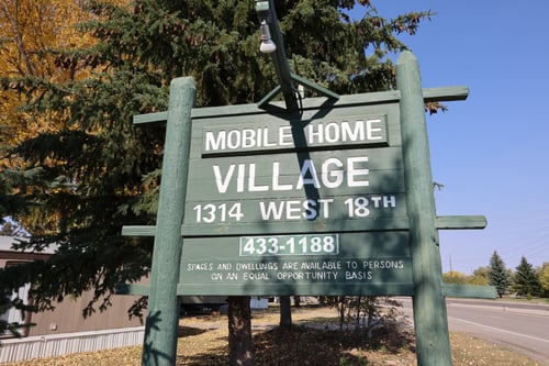 A green sign for Mobile Home Village in front of a mobile home.