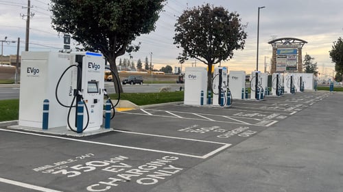 Several EVgo fast-charging units installed in marked parking spaces at a public charging station, with EVgo logos on the chargers, protective bollards around each unit