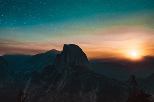 Mountain silhouette at sunset with golden sky and stars.