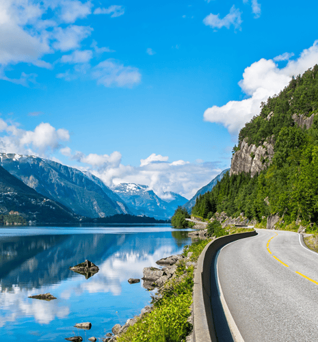 A curved road beside a calm lake, surrounded by mountains.
