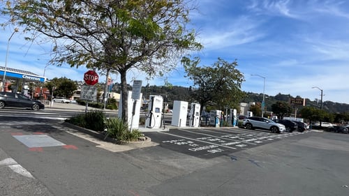 Several EVgo fast-charging units installed in marked parking spaces at a public charging station, with EVgo logos on the chargers, protective bollards around each unit