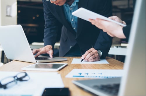 Business meeting with two people focusing on laptops and documents on a wooden table, conveying a professional and collaborative atmosphere.