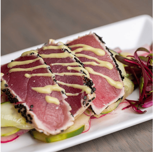 Sesame-crusted seared tuna slices with creamy sauce, served over cucumbers and radishes at Outer Banks Steamers.