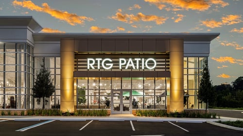 Exterior of the Rooms To Go Patio showroom at sunset, featuring a modern design with large windows, a well-lit entrance