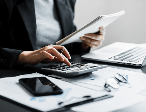 Close up of a person working at a desk with a calculator, laptop, phone, and financial documents.