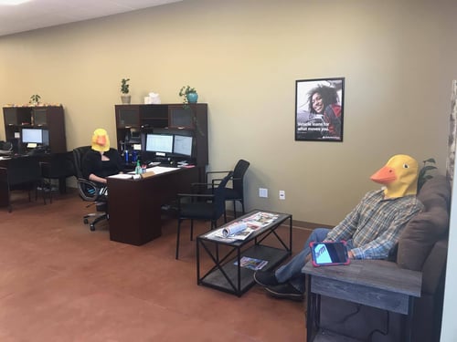 Two people sitting and wearing chicken heads in our office