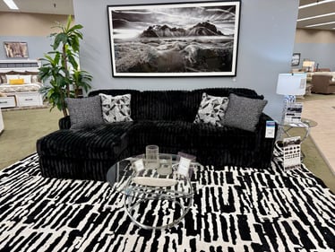 Modern black corduroy Midnight Madness sectional sofa with patterned rug and wall art display at Slumberland Furniture Burlington. Visit our Burlington, Iowa showroom for trendy and cozy living room furniture.