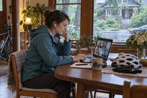 Woman joins a video call from her Portland home, with a commuter bicycle by the door and a helmet and gloves ready on the table.