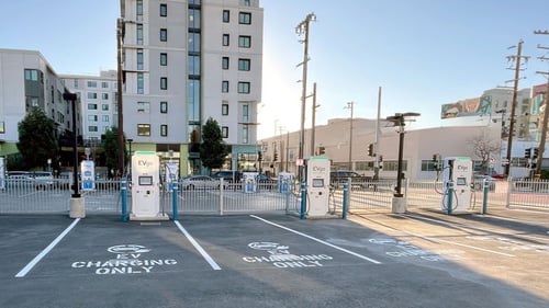 Several EVgo fast-charging units installed in marked parking spaces at a public charging station, with EVgo logos on the chargers, protective bollards around each unit