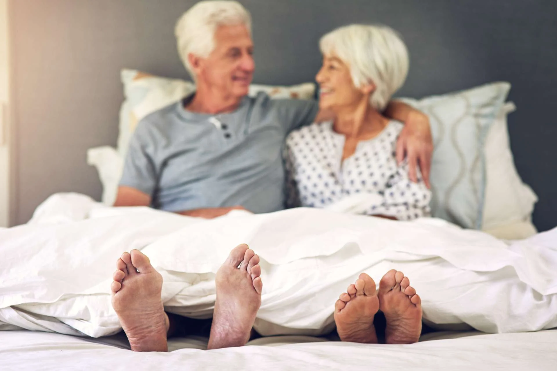 elderly couple in bed with their feet peeking out under the covers