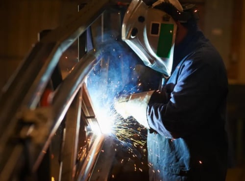 Industrial welder performing arc welding on metal structure with sparks.