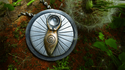 Amulett aus Silber mit einer drehbaren Scheibe auf der sich eine urtümliche Darstellung der Großen Göttin befindet mit Spirale im Unterleib und einem grünen leuchtenden Mondstein als Kopf