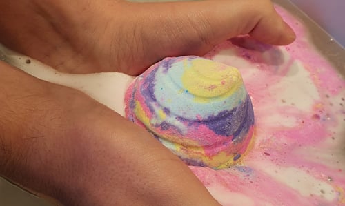 Colourful Unicorn Poop Bath bomb being held in the water.