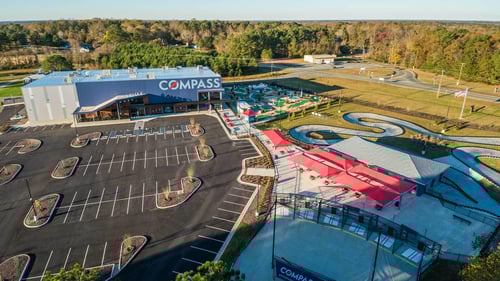 Overhead view of Compass Entertainment Complex including go-kart track, miniature golf course, batting cages, movie theater, bar and grill, and indoor family entertainment center.