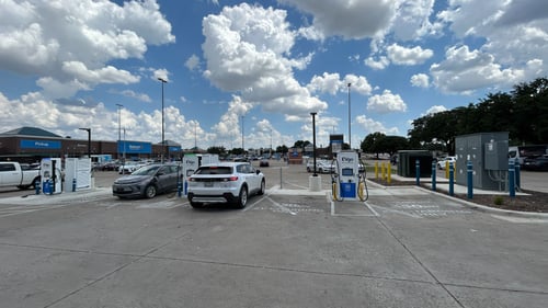 Several EVgo fast charging units installed in marked parking spaces at a public charging station, with EVgo logos on the chargers, protective bollards around each unit.
