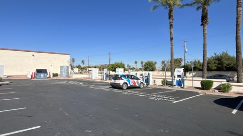 Several EVgo fast-charging units installed in marked parking spaces at a public charging station, with EVgo logos on the chargers, protective bollards around each unit