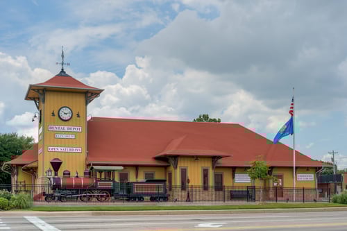 Exterior view of Dental Depot's Norman dentist office with a clock tower, model train, and yellow walls.