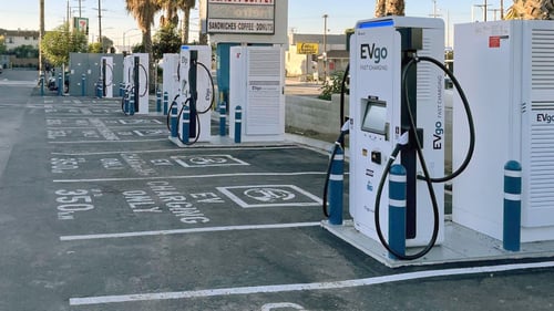 Several EVgo fast-charging units installed in marked parking spaces at a public charging station, with EVgo logos on the chargers, protective bollards around each unit