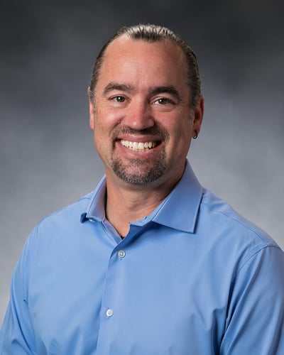 Timothy DeVries, PA-C smiling in front of a gray background.