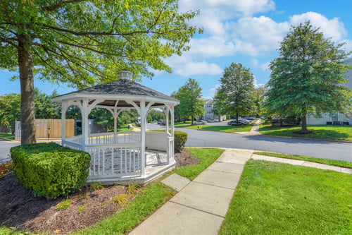 A white gazebo with a black roof is surrounded by greenery and a sidewalk at Acclaim at Sterling in Sterling, Virginia